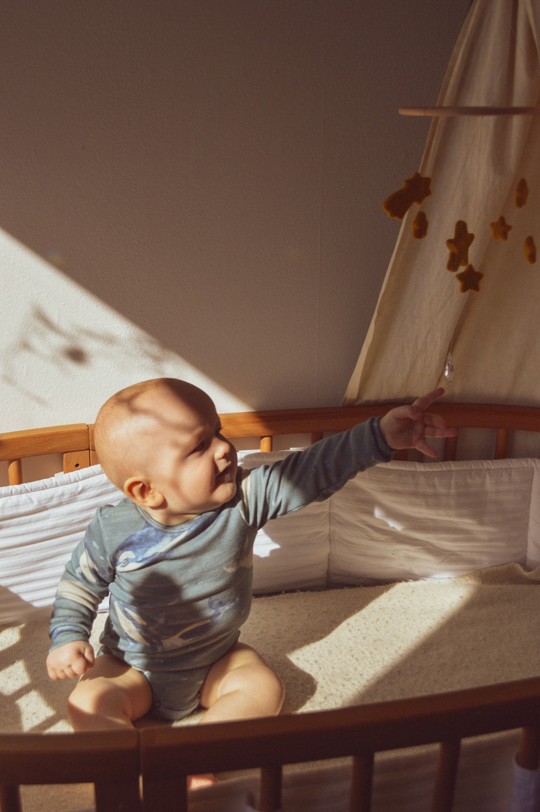 Baby sitzt im Bett mit handgenähtem Body